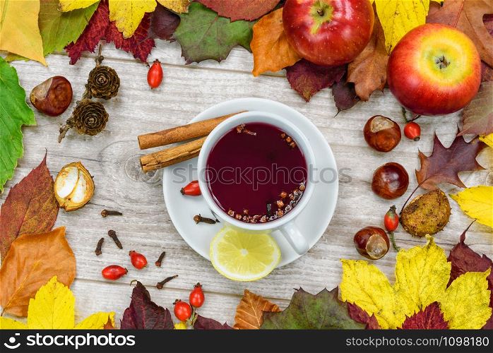 A cup of warm tea with wild rose with spices and lemons and surrounded by autumn rustic decoration.