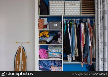 A cupboard with the usual sloppy man&rsquo;s belongings, next to it stands an ironing board
