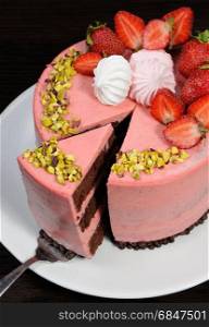 A cut piece of chocolate strawberry mousse cake decorated with berries, meringue and pistachios