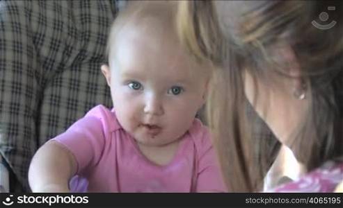 "A cute 10-month-old baby smiles then takes a bite, as her mom does the "airplane" with the spoon."