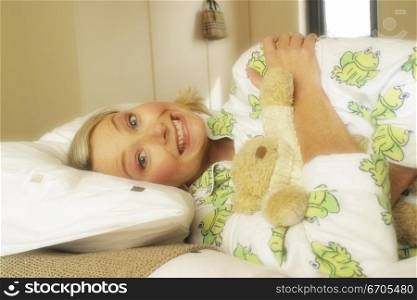 A cute 30&acute;s woman in bed sleeping and cuddling a teddy bear. She is wearing her pajamas
