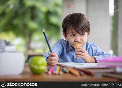 A cute boy eating with ice cream cone during homework breaks at home during covid 19 lock down,Home schooling,Social Distance.