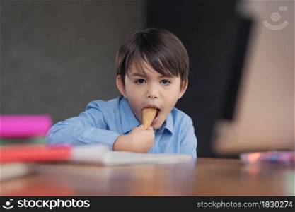 A cute boy eating with ice cream cone during homework breaks at home during covid 19 lock down,Home schooling,Social Distance.