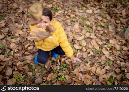 A cute boy in winter coat throwing leaves in an autumn season.