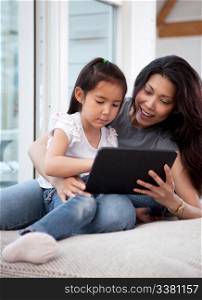 A cute happy mother and daughter using a digital tablet at home in the living room