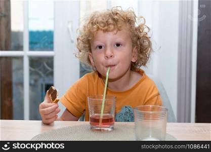 a cute little boy is drinking red juice using straw
