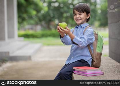 A cute little boy wearing a blue shirt and carrying a student backpack receive apple from mother for breakfast before go to school.Breakfast is important for child development.health and wellness.