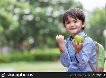 A cute little boy wearing a blue shirt and carrying a student backpack holding happle and showing bicep muscles.Child with confidence ready to defense from bullying.Ready to go school again.