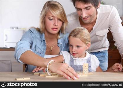 A cute little girl playing dominos with her parents.