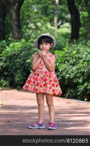 A cute smiling little girl in a red floral dress is walking and having fun on the green grass in the park. childhood concept