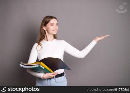 A cute student girl holds notebooks for notes and points to the side with her hand.. A cute student girl holds notebooks for notes and points to the side with her hand