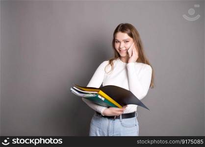 A cute student girl is talking on the phone and holding an open folder for documents.. A cute student girl is talking on the phone and holding an open folder for documents