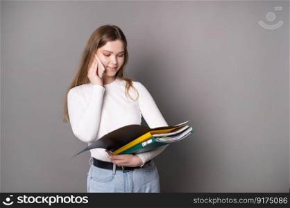 A cute student girl is talking on the phone and looking at an open folder for documents.. A cute student girl is talking on the phone and looking at an open folder for documents