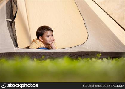 A cute white boy lay with his hands on his chin looking out of the tent.