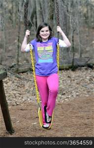 A cute young girl standing on a swing smiling.