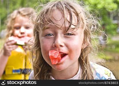 A cute young girl with a messy face playing in the water and eating watermelon.