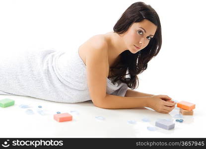 a cute young woman with dark hair and fair skin laying down on the floor near colorated soap and petals