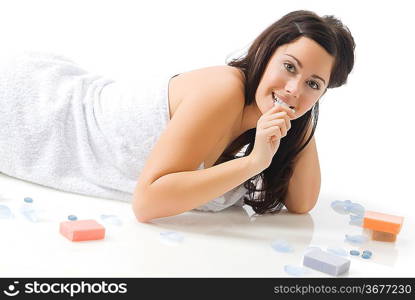 a cute young woman with dark hair and fair skin laying down on the floor near colorated soap and petals