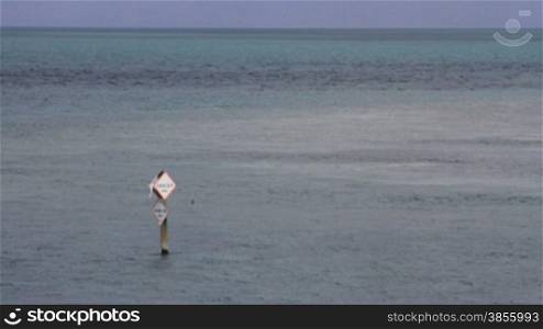 A danger sign sticks out of the water in a vast body of water, warning of a shoal, in the Florida Keys