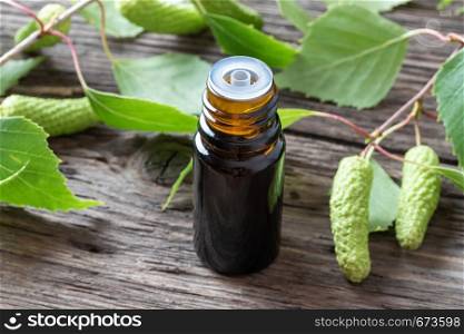 A dark bottle of essential oil with fresh birch branches