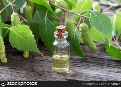 A dark bottle of essential oil with fresh birch branches