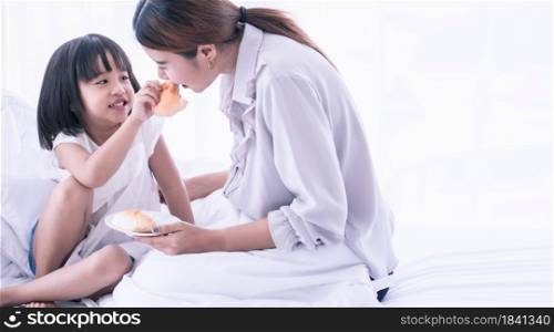 A daughter giving a bread to her mom while having breakfast on bed in the morning