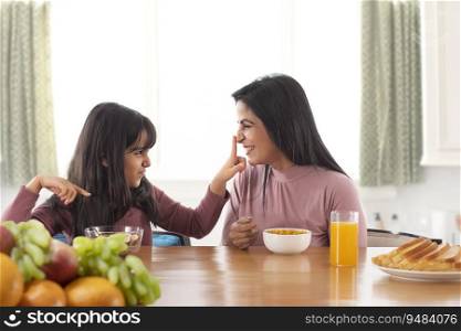 A DAUGHTER HAPPILY PLAYING WITH MOTHER WHILE HAVING BREAKFAST