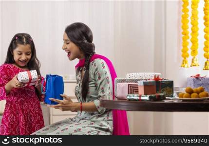A daughter overjoyed at gift given by mother amidst presents,sweets and festive flower garland decoration.