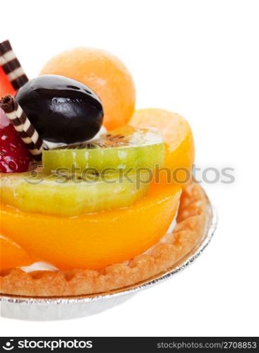 A decadent fruit tart, piled high with fresh fruit, and garnished with two delicate spikes of rolled white and milk chocolate. Shot on white background with shallow depth of field.