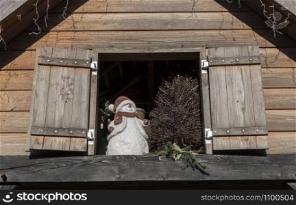 a decoration snowman with hat looking out of the window in a wooden house