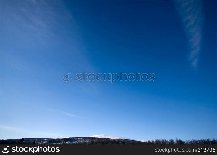 A deep blue sky background with faint clouds and a sliver of mountains
