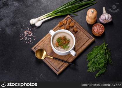 A delicious fresh, thick soup ofμshroom puree with breadcrumbs, sπces and herbs on a wooden board against a dark concrete background. Ve≥tarian cuisi≠. A delicious fresh, thick soup ofμshroom puree with breadcrumbs, sπces and herbs