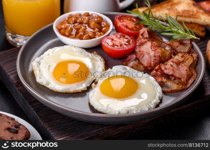 A delicious nutritious healthy breakfast with fried eggs, bacon, beans, a glass of juice, oat cookies, milk and jam. Healthy eating at the beginning of the day. A delicious nutritious healthy breakfast with fried eggs, bacon, beans, a glass of juice, oat cookies, milk and jam