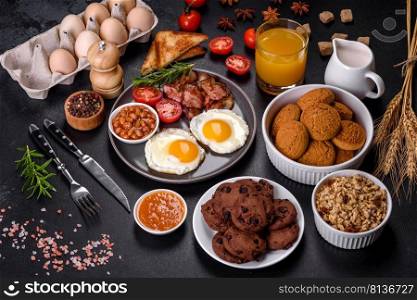 A delicious nutritious healthy breakfast with fried eggs, bacon, beans, a glass of juice, oat cookies, milk and jam. Healthy eating at the beginning of the day. A delicious nutritious healthy breakfast with fried eggs, bacon, beans, a glass of juice, oat cookies, milk and jam