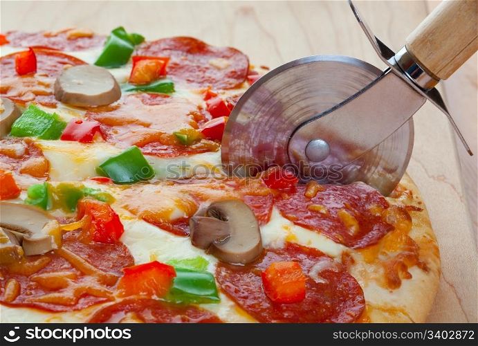 A deluxe pizza, fresh from the oven, being cut up for serving.