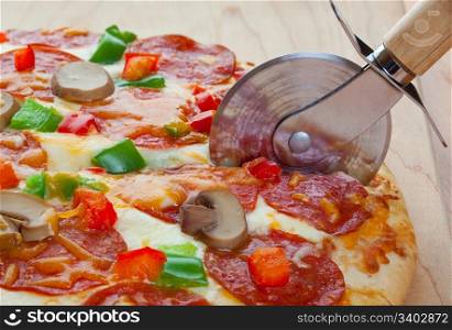 A deluxe pizza, fresh from the oven, being cut up for serving.