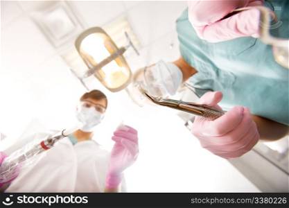 A dentist and assistant pulling teeth from the viewers mouth, focus on the pulled tooth