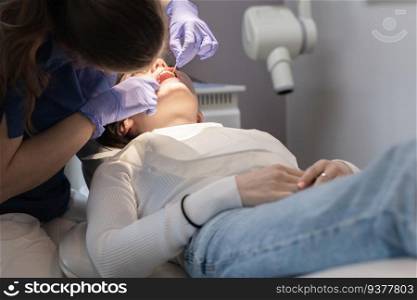 A dentist doctor in lilac gloves examines the oral cavity with a tool to a young girl patient lying in a chair, close-up side view. Concept, health and oral hygiene.. The dentist examines the oral cavity of the patient.