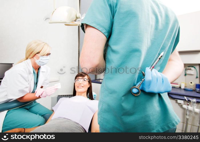 A dentist with a big needle behind his back and a worried patient