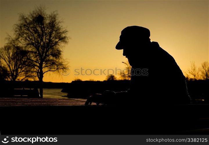 A depressed thoughtful man by the water at sundown. Warm sunlight creating a silhouette.