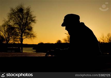 A depressed thoughtful man by the water at sundown. Warm sunlight creating a silhouette.