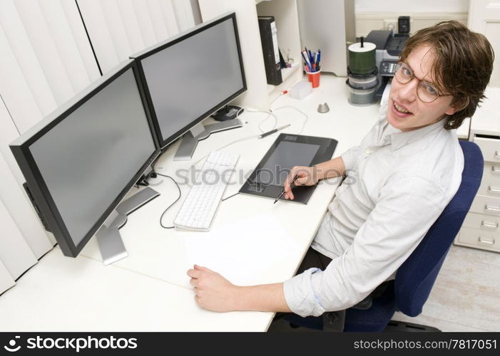 A designer at work behind two monitors, looking up at the camera