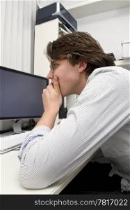 A designer staring in deep concentratio at his computer screens, elbow on the table, chin resting in his hand