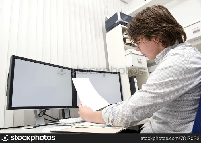 A designer, studying a ducument from the thick file in front of him behind his desk