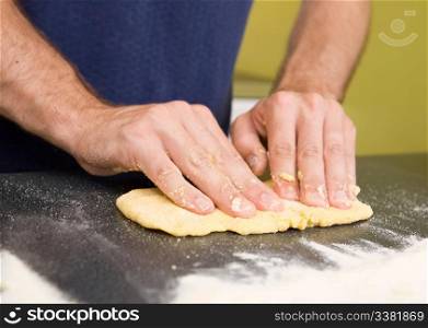 A detail image of a male making fresh pasta on the counter. The pasta dough is being flatened before rolling through the pasta machine
