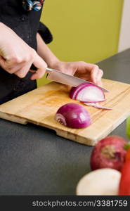 A detail image of a woman cutting a red onion at home in the kitchen.