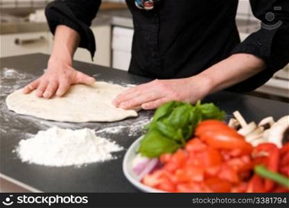 A detail image of a woman making pizza dough on the kitchen counter. Shallow depth of field is used with the focus on the hands and dough.