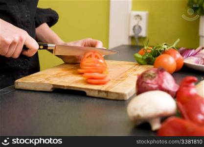 A detail image of a woman slicing tomatoes on a cutting board at home. - shallow depth of field with the focus on the tomato and knife