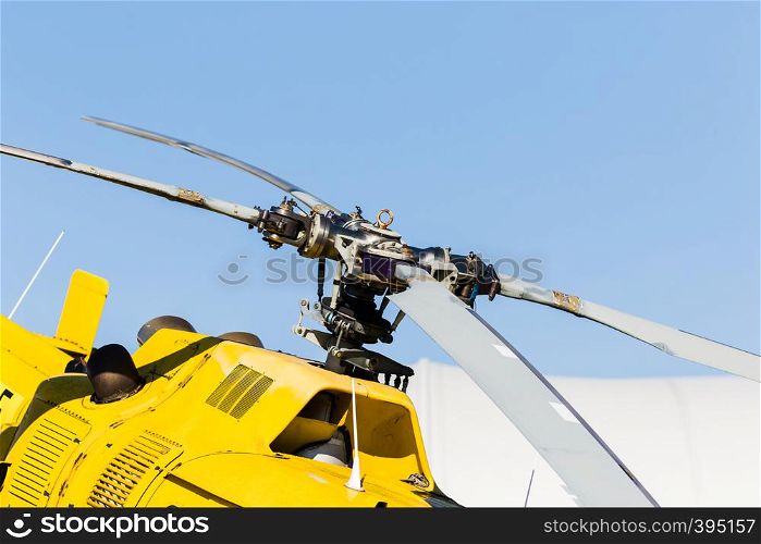 A detail of the rotor of a yellow helicopter with the sky in the background