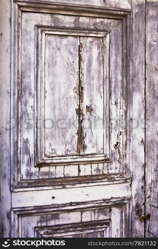 A detail view of an old, weather-beaten wood door with layers of peeling gray paint results in a distressed, weathered texture.